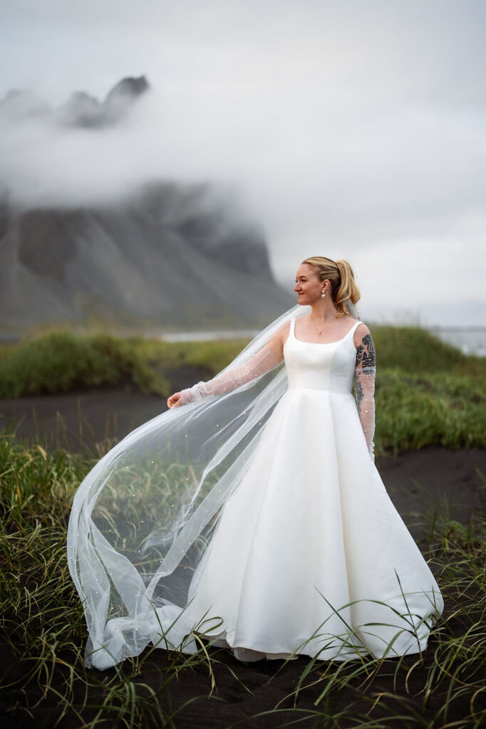 bride stands with veil in the wind during iceland wedding day.