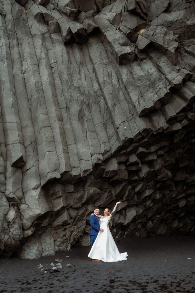 bride and groom stand under rock formations during adventure elopement with iceland wedding photographer.
