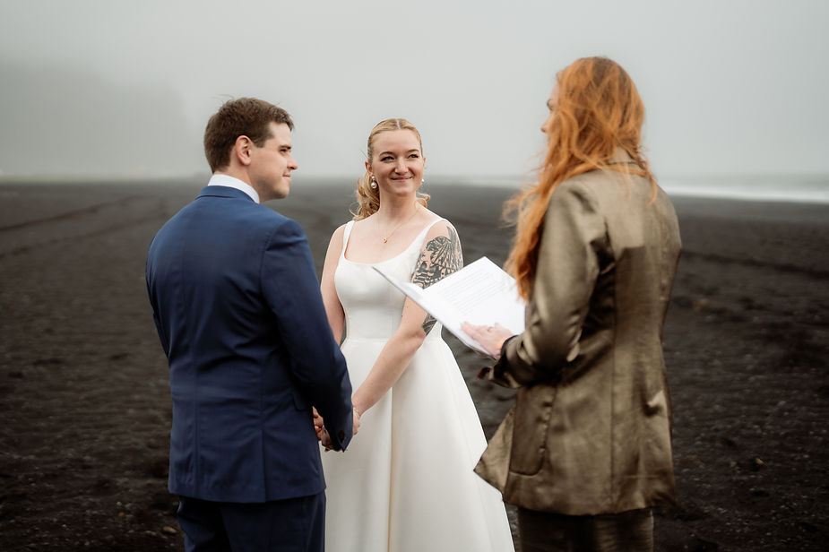 bride and groom stand on black sand beach during iceland wedding ceremony.