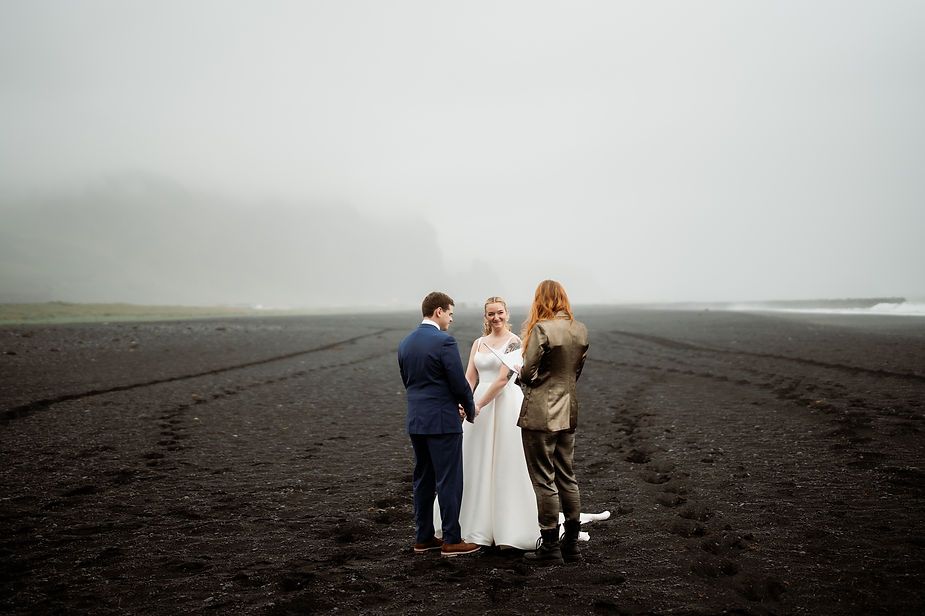 bride and groom stand on black sand beach during iceland wedding ceremony.