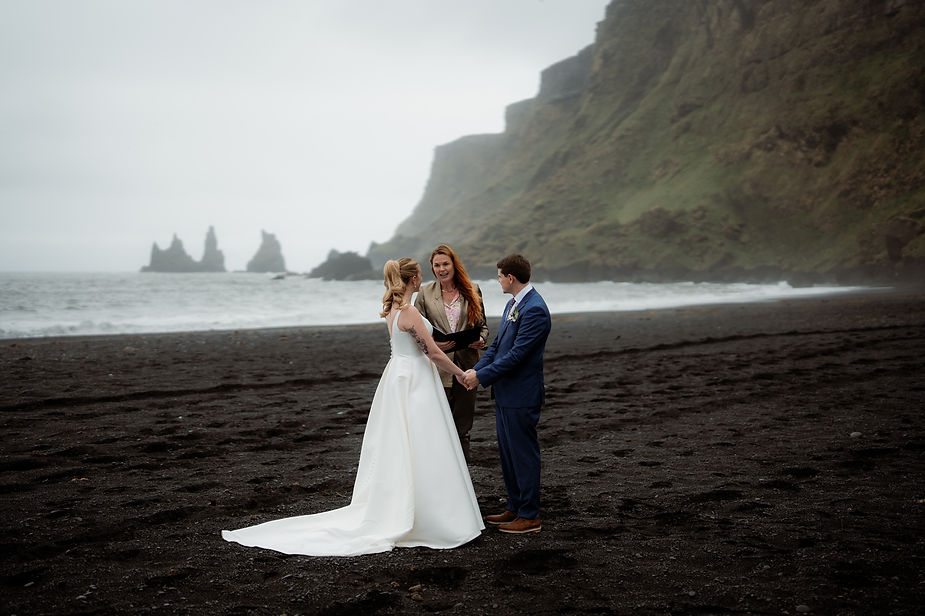 bride and groom stand on black sand beach during iceland wedding ceremony.