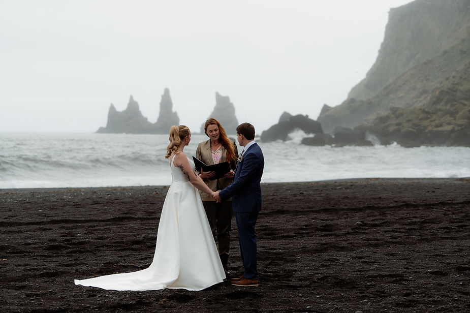 bride and groom stand on black sand beach during iceland wedding ceremony.