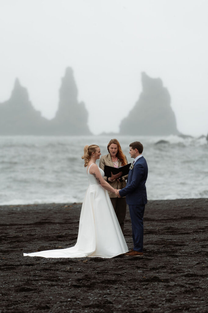 bride and groom stand on black sand beach during iceland wedding ceremony.