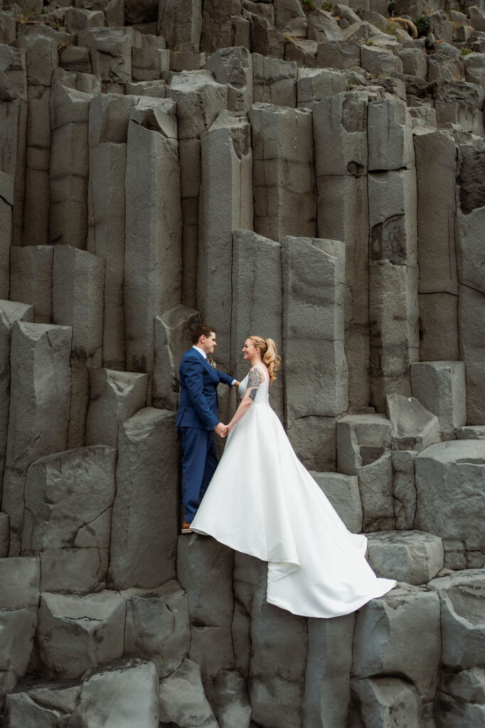 bride and groom stand on rock formations during iceland wedding day adventure with photographer.