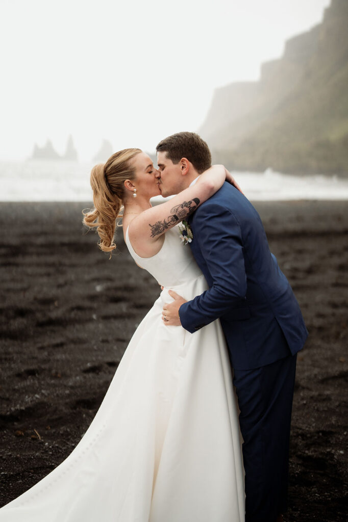 bride and groom kiss on black sand beach during adventure wedding in iceland with elopement photographer.