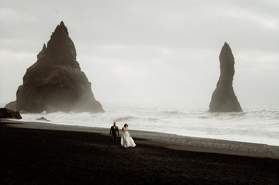 bride and groom walk along black sand beach during their honeymoon in iceland.