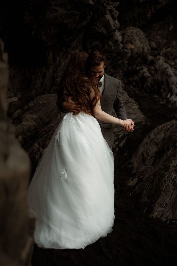 bride and groom dance beside rock formations during iceland honeymoon.