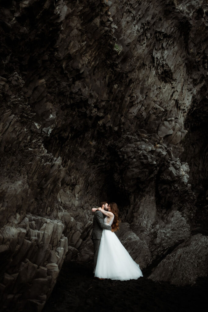bride and groom hug beside rock formations during photo shoot with iceland elopement photographer.