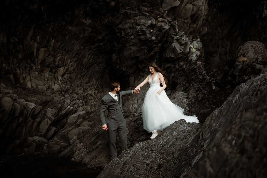 Bride and groom climb on rock formations during iceland honeymoon.