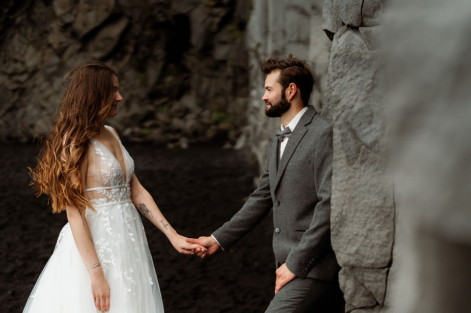 bride and groom lean on rock formations and hold hands during iceland honeymoon.