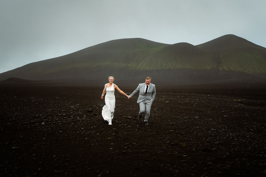 bride and groom run through valley in iceland.