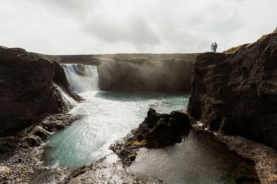 bride and groom stand on ledge over valley in iceland.