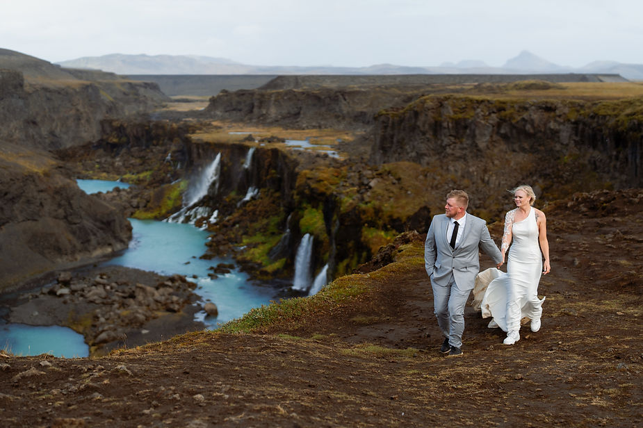 bride and groom walk along edge of valley during iceland wedding day.