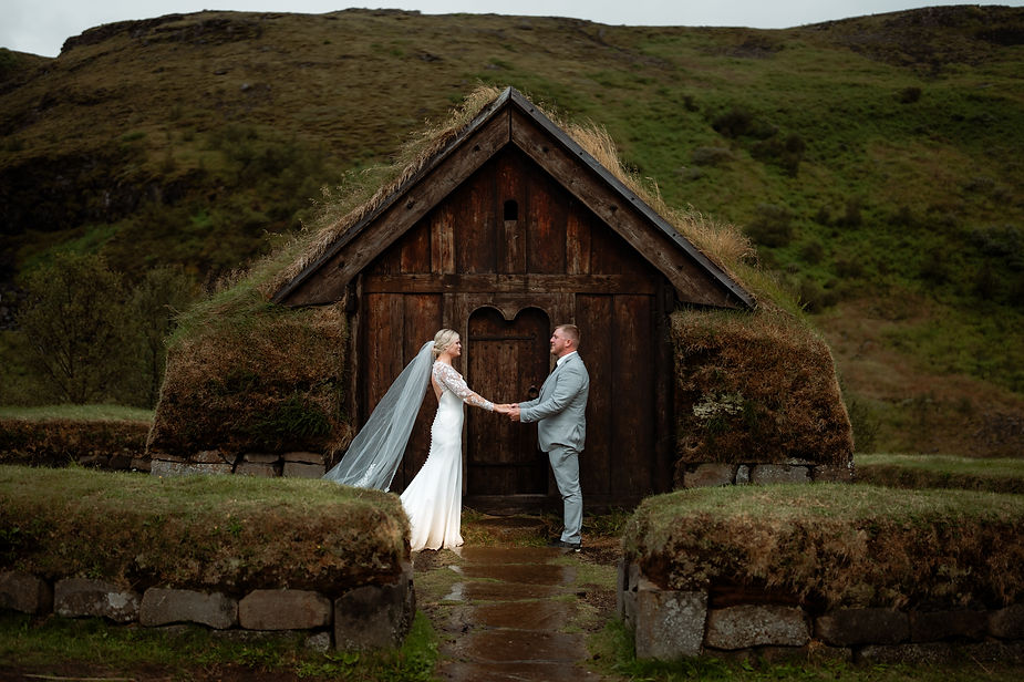 bride and groom stand and hold hands in front of old viking house during wedding photos in iceland.
