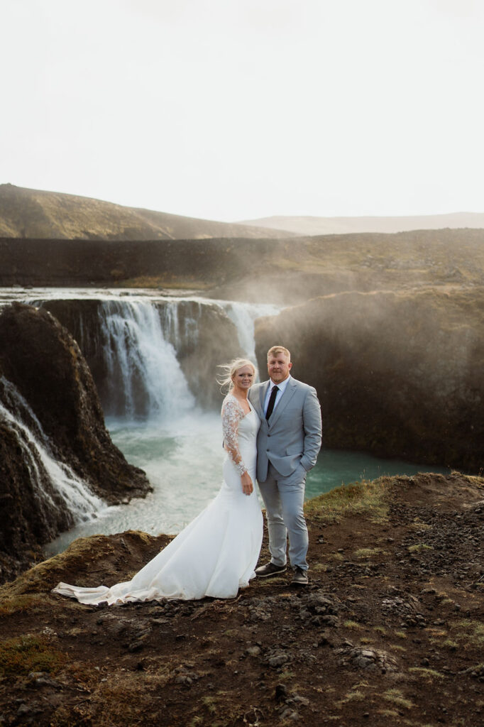 bride and groom stand in front of waterfall during iceland wedding day.