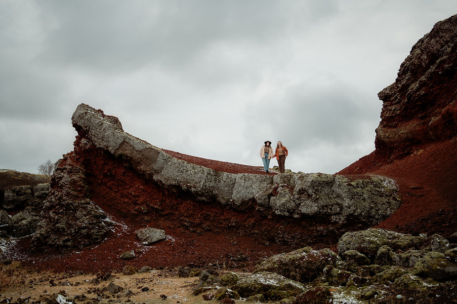 lgbtq+ couple stand on rock formation near reykjavik during their adventure proposal photos.