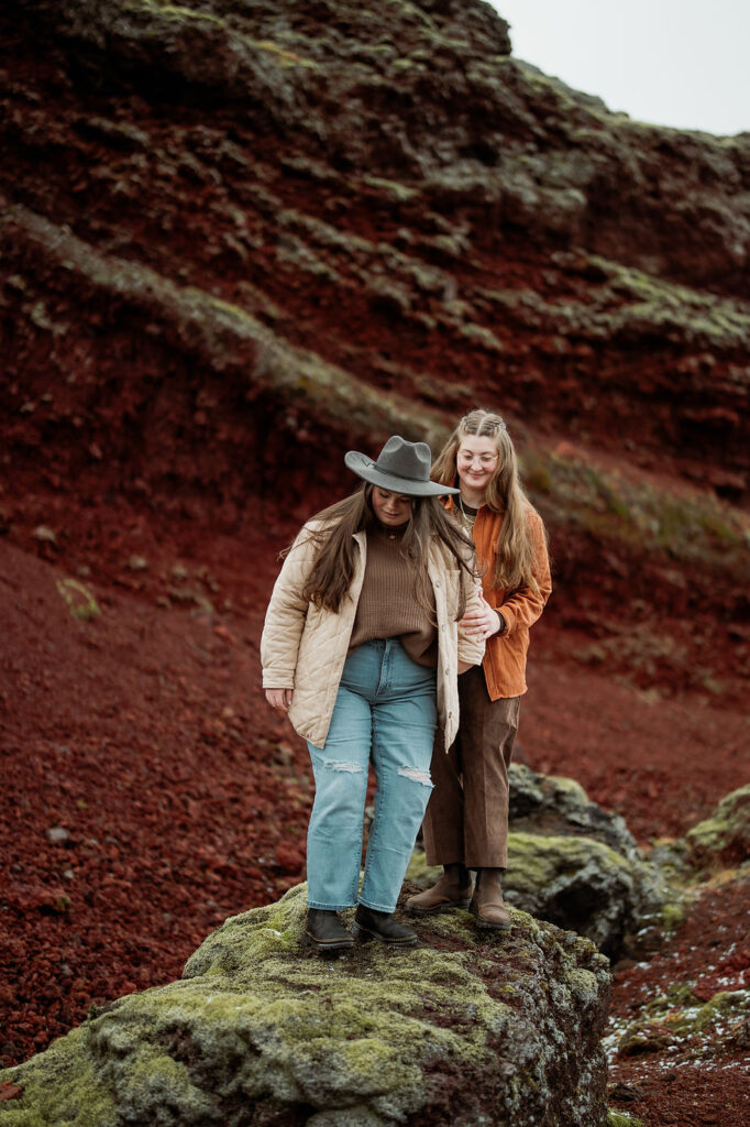 lgbtq+ couple walks down mossy ledge during adventure proposal photos in iceland.