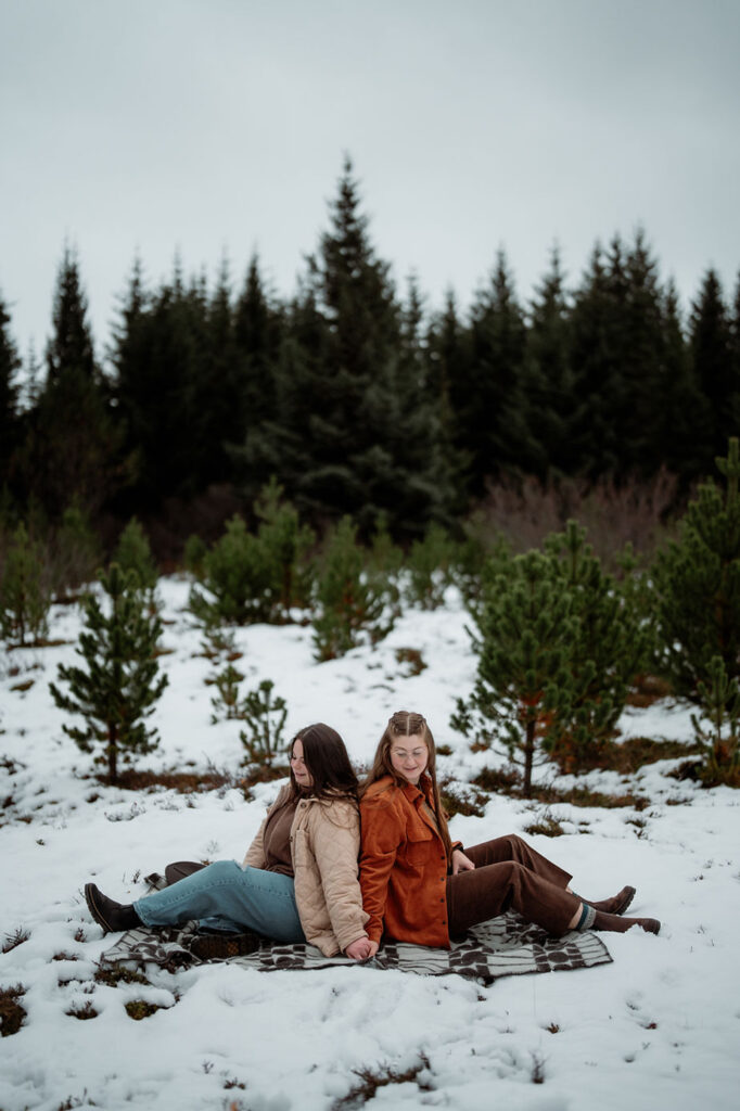 lgbtq+ couple sit on blanket during iceland proposal photo shoot.