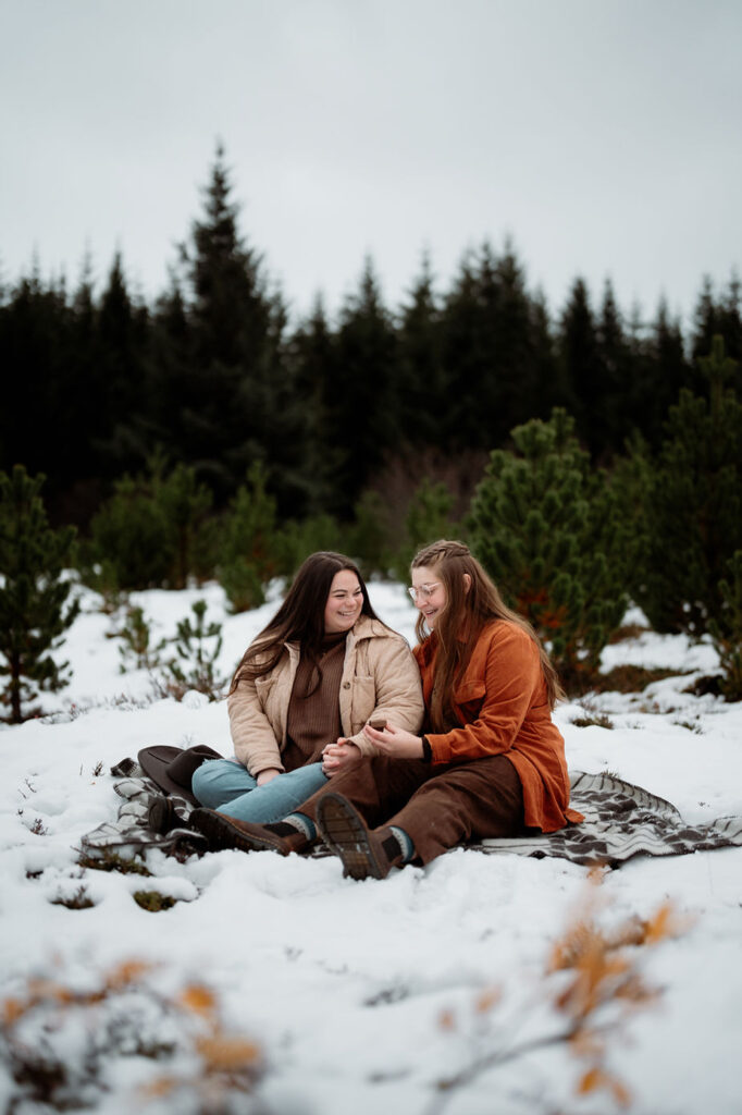lgbtq+ couple sits on blanket and look at engagement ring after iceland proposal.