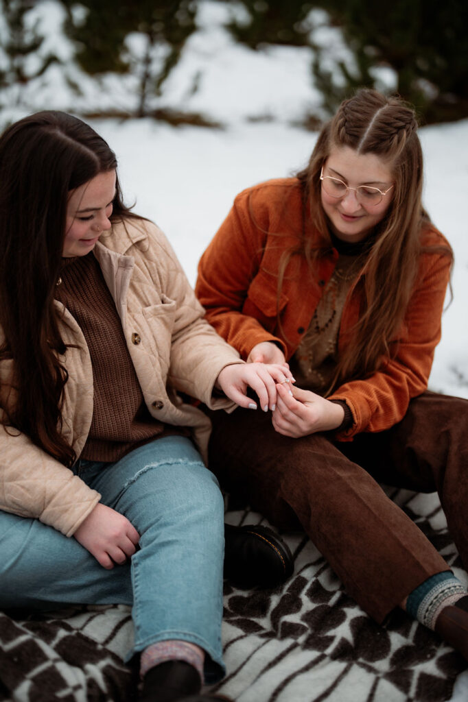 lgbtq+ couple sits on blanket and puts engagement ring on, during iceland proposal photos.