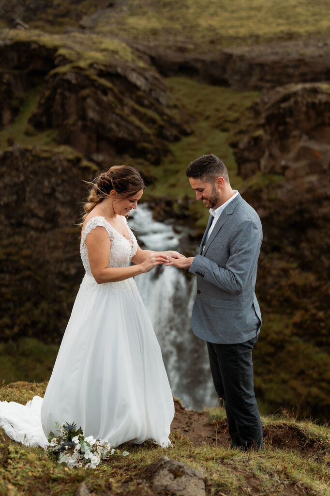 groom puts wedding ring on brides finger during destination wedding in iceland.