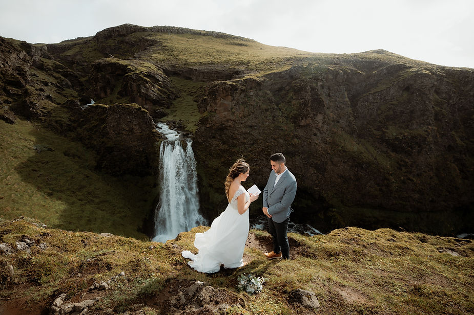 bride and groom read wedding vows overlooking an iceland valley and waterfall.