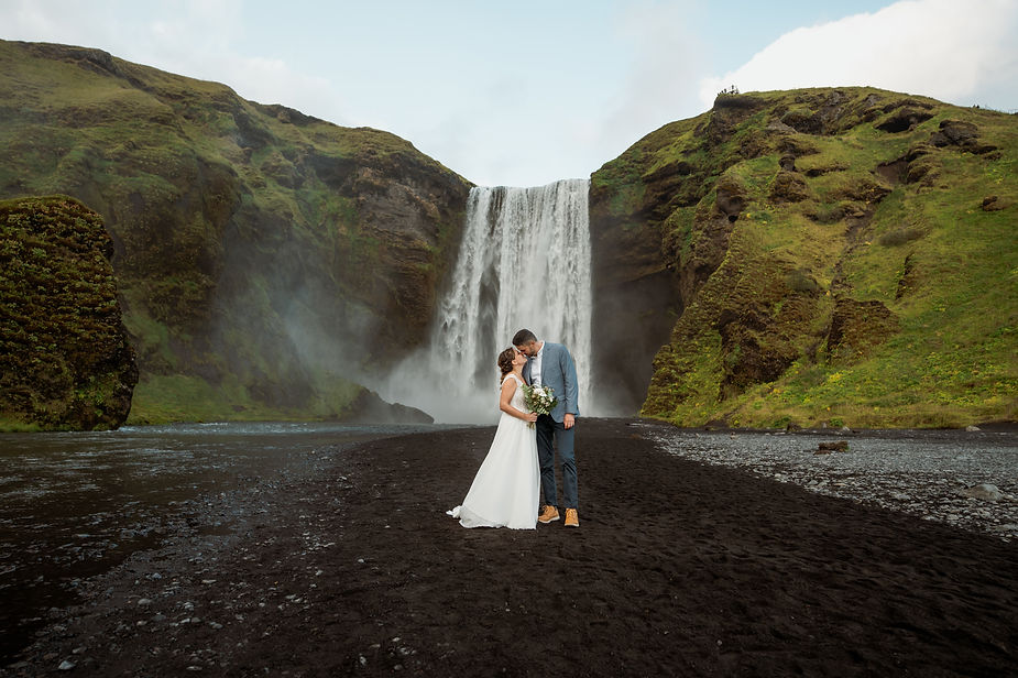bride and groom kiss in front of iceland valley and waterfall.