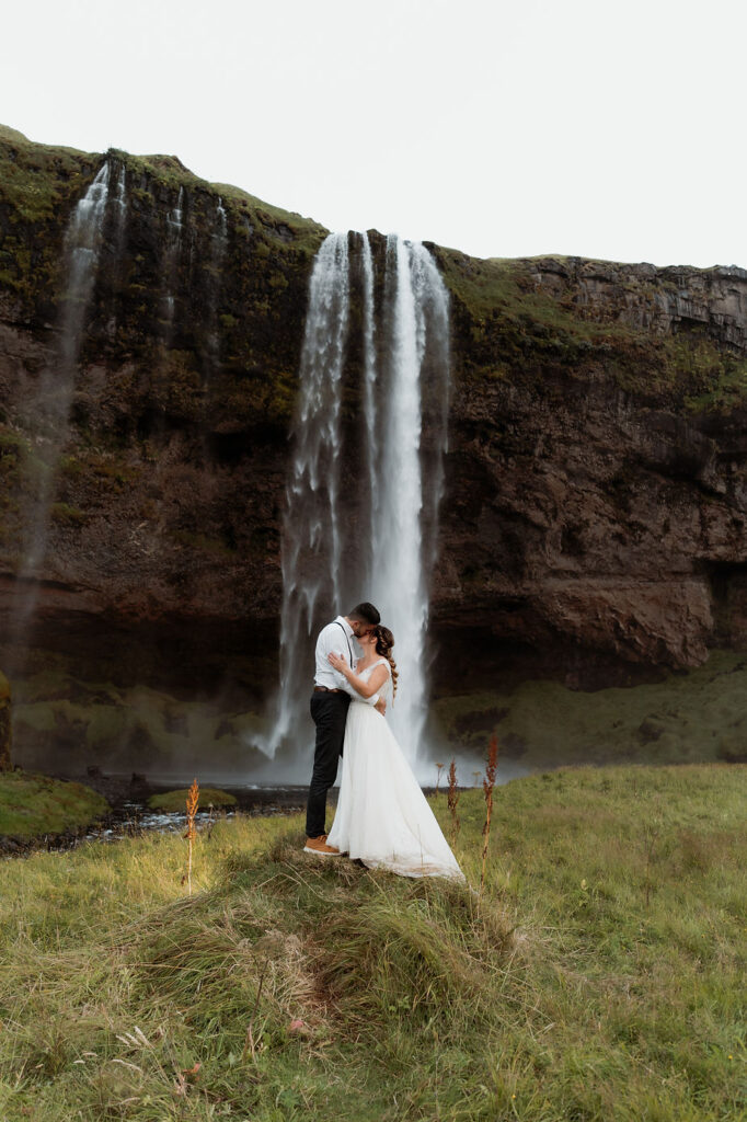 bride and groom embrace in front of iceland waterfall during elopement day.