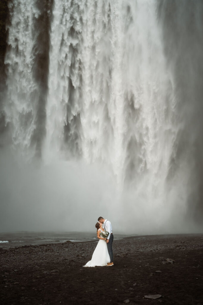 bride and groom kiss in front of waterfall in iceland.