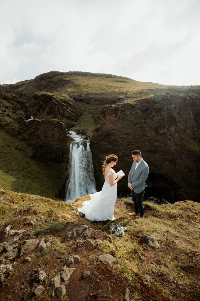 bride and groom read vows over valley during iceland elopement.