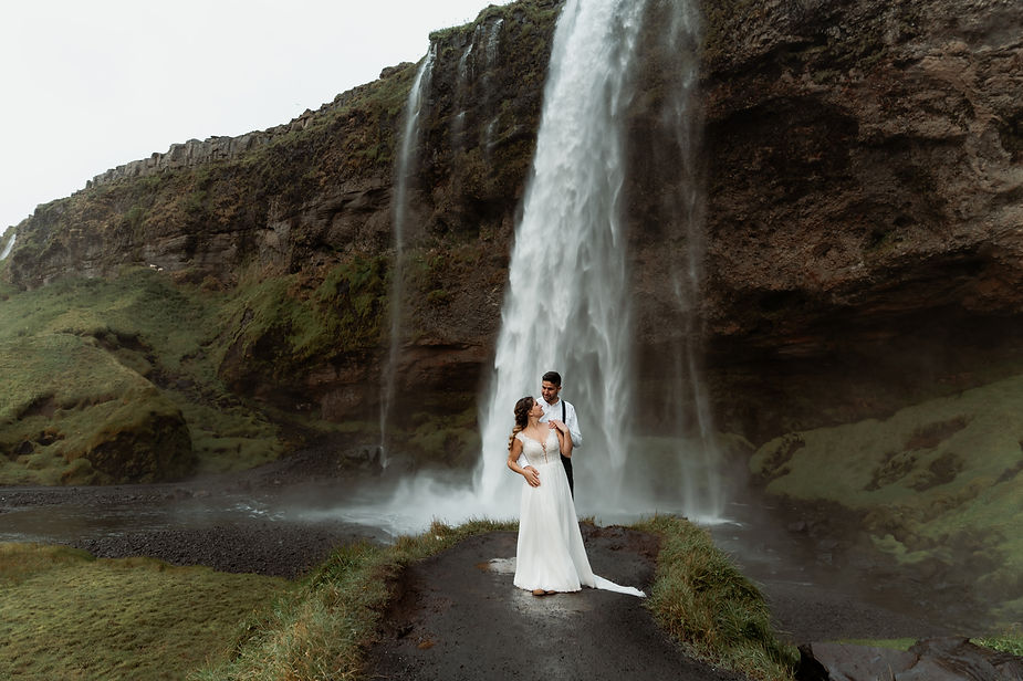 bride and groom stand in front of waterfall during iceland wedding.