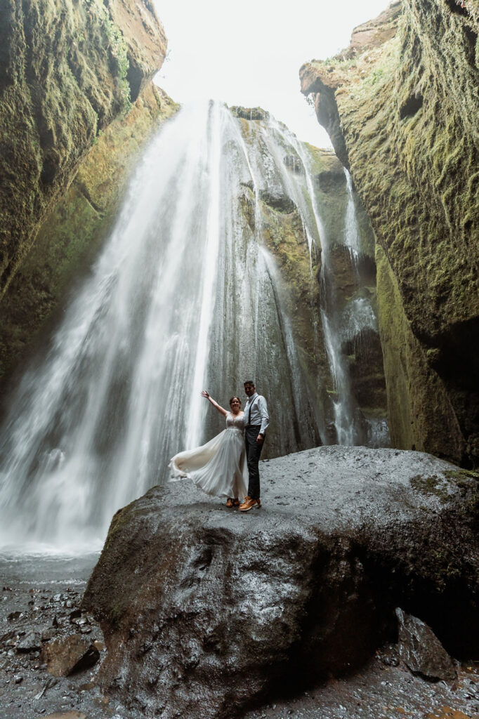 bride and groom stand on rock in front of waterfall during iceland elopement.