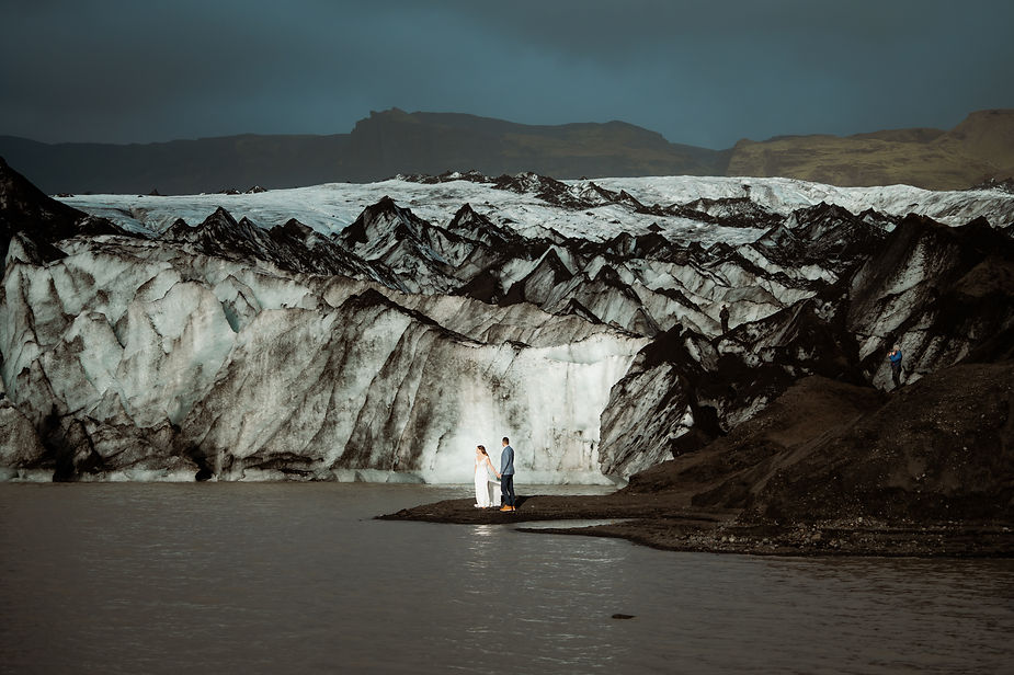 bride and groom walk along shore in front of glacier during their adventure elopement in iceland.