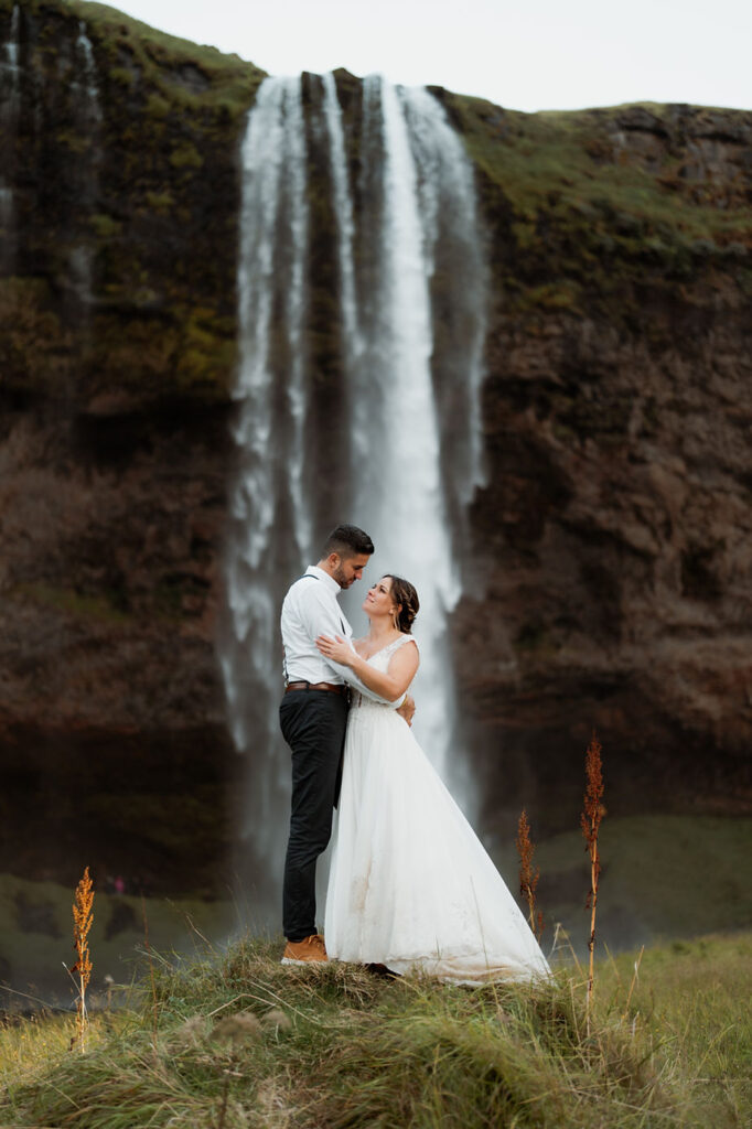 bride and groom stand in front of waterfall during iceland wedding day.