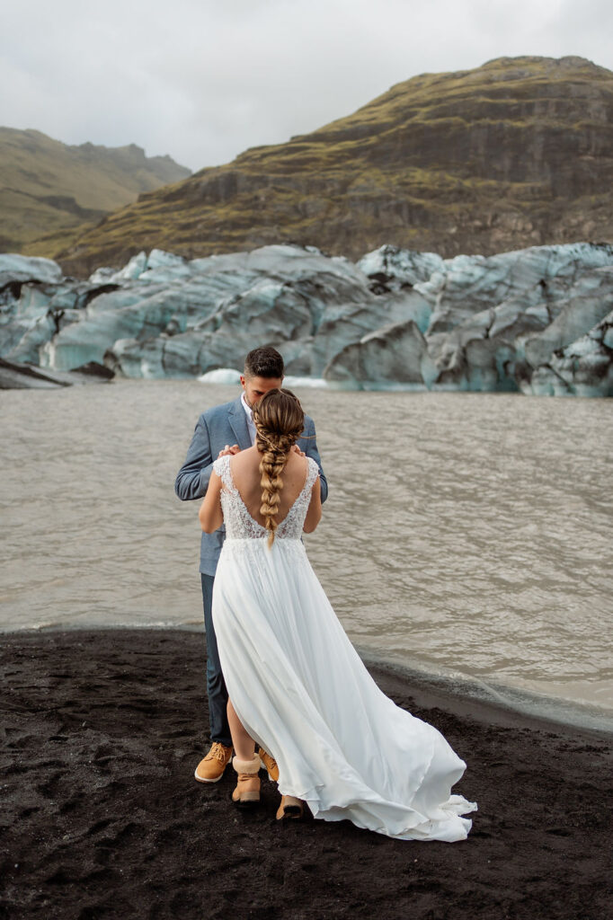 bride and groom stand on black sand in front of glacier during iceland elopement adventure.