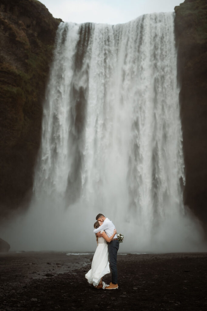 bride and groom pose for iceland elopement photographer in front of a waterfall.