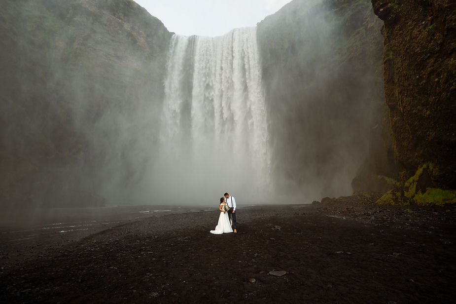 bride and groom stand in front of waterfall during iceland adventure elopement.